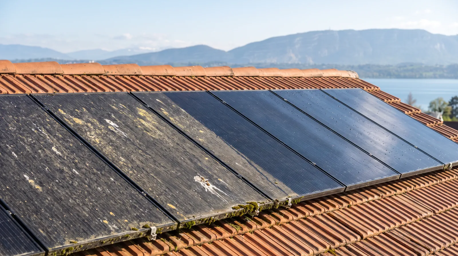 Panneaux solaires sur un toit face au lac Léman et au Salève, à moitié nettoyés